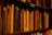 A close-up view of a bookshelf filled with old, worn books. The book spines are visible, many without titles, suggesting age and heavy use. The lighting is warm and dim, creating a cozy and nostalgic atmosphere. A small sign in Polish reads 'książki wydane do 1939 r.', indicating that the books were published before 1939.