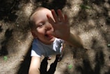 A young child smiling brightly while reaching out during a playful physiotherapy session.
