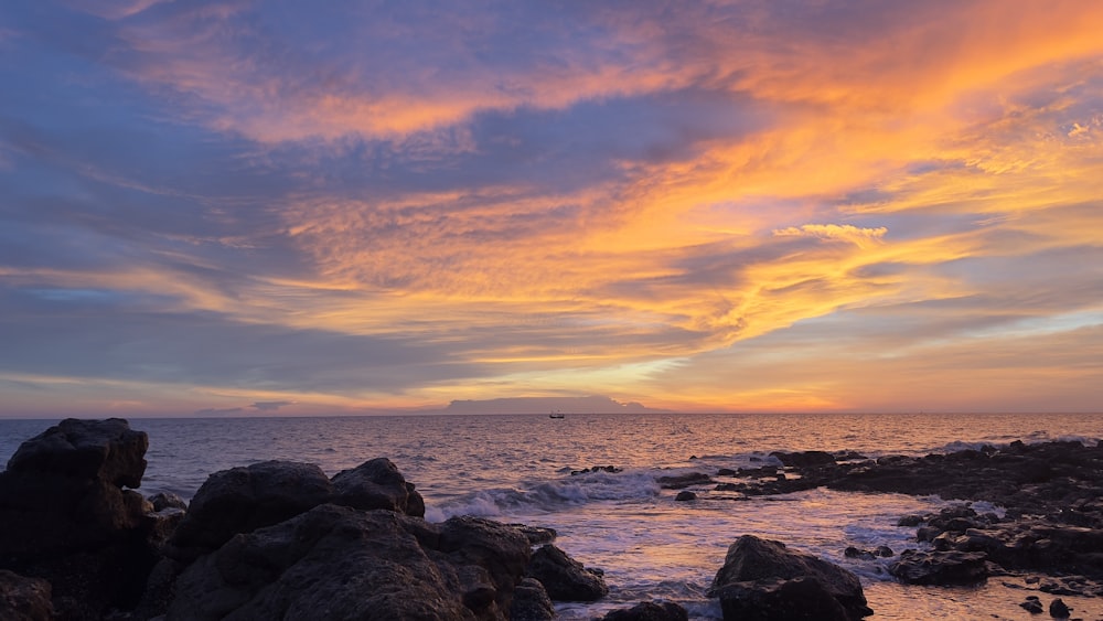 a sunset over the ocean with rocks and water