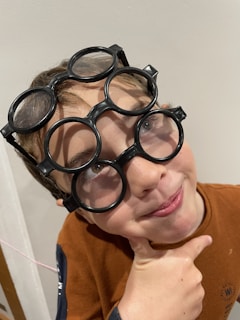 A boy smiling while trying on different sunglasses in a store.