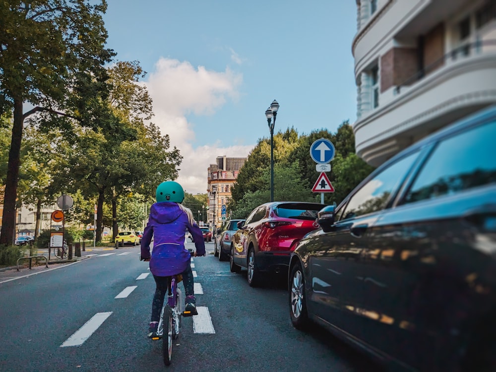 eine Frau, die mit dem Fahrrad eine Straße neben geparkten Autos entlangfährt