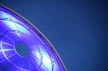 A circular, geometric structure glows with a bright blue light against a deep blue background. The structure appears to be part of a larger framework, with visible spokes or beams radiating from a central circular opening.