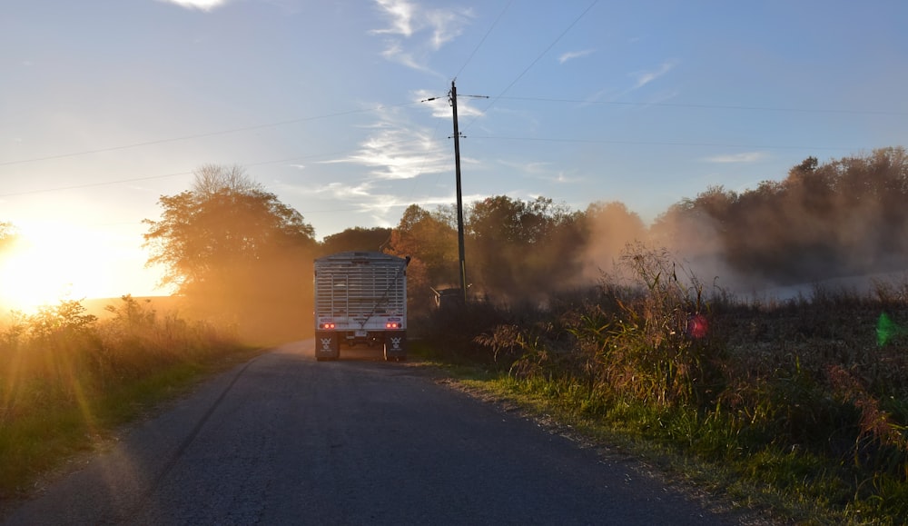 a truck driving down a country road at sunset