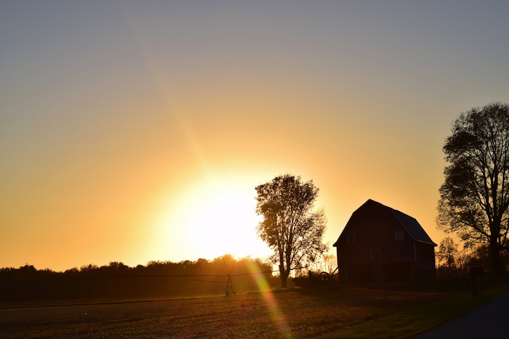 the sun is setting behind a barn and trees