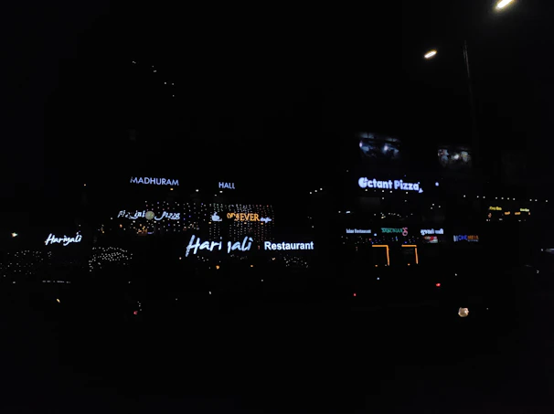 Brightly lit glow-sign business board hanging outside a busy shop in Ongole.