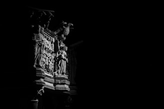 A detailed stone carving is illuminated by a strong light source, highlighting an intricate scene with figures and ornate decorations. The carving displays human forms and an eagle, with deep shadows creating a dramatic contrast.