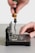 A hand is using a screwdriver to work on an open electronic device, possibly a hard drive or similar component. The device is positioned on a flat surface, and intricate parts and circuit boards are visible inside.