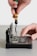 A hand is using a screwdriver to work on an open electronic device, possibly a hard drive or similar component. The device is positioned on a flat surface, and intricate parts and circuit boards are visible inside.