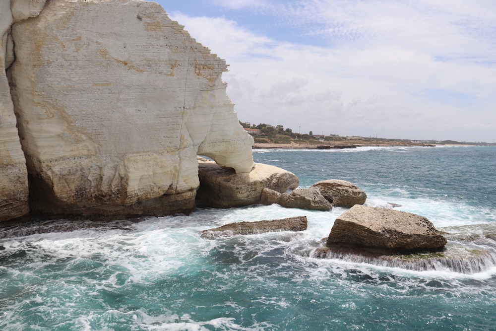 a large rock sticking out of the ocean next to a cliff