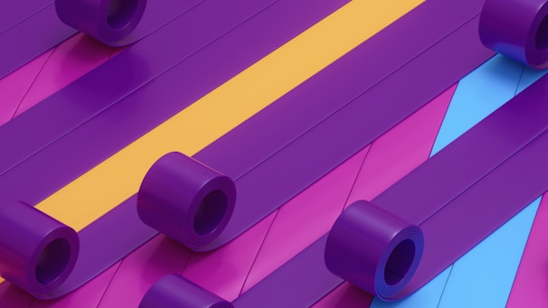 Multiple rolls of colorful plastic material are unrolled and laid out parallel to each other. The materials display a vibrant color scheme with prominent purple, yellow, and blue tones.