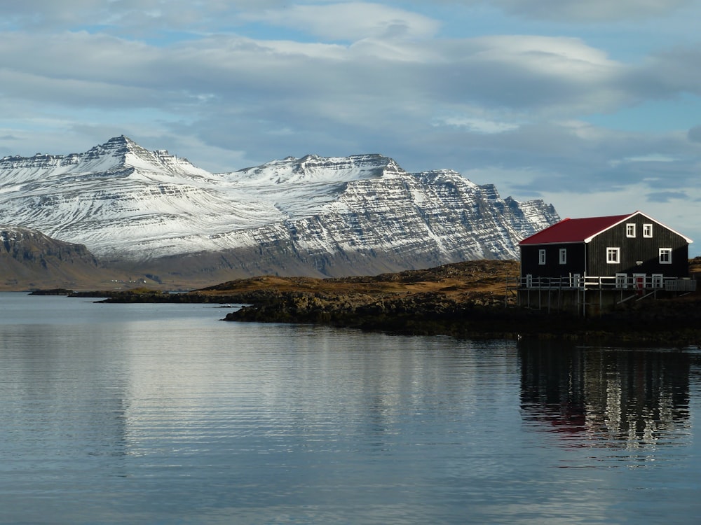 a house on the shore of a lake with mountains in the background