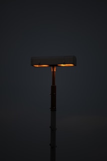 A single streetlamp with two rectangular lights illuminated with a warm glow, standing against a dark background.
