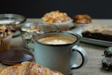 Fresh pastries displayed next to a cup of cappuccino on a cream-colored surface.