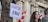 A young person with long hair stands in front of a building with Canadian flags. Next to them, a tree has a sign attached that reads 'Ceasefire Now!' in bold letters.