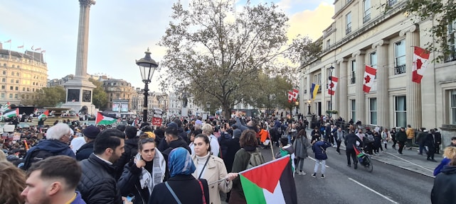 A diverse group of people holding Dutch flags, standing together in a city square, symbolizing unity and hope.