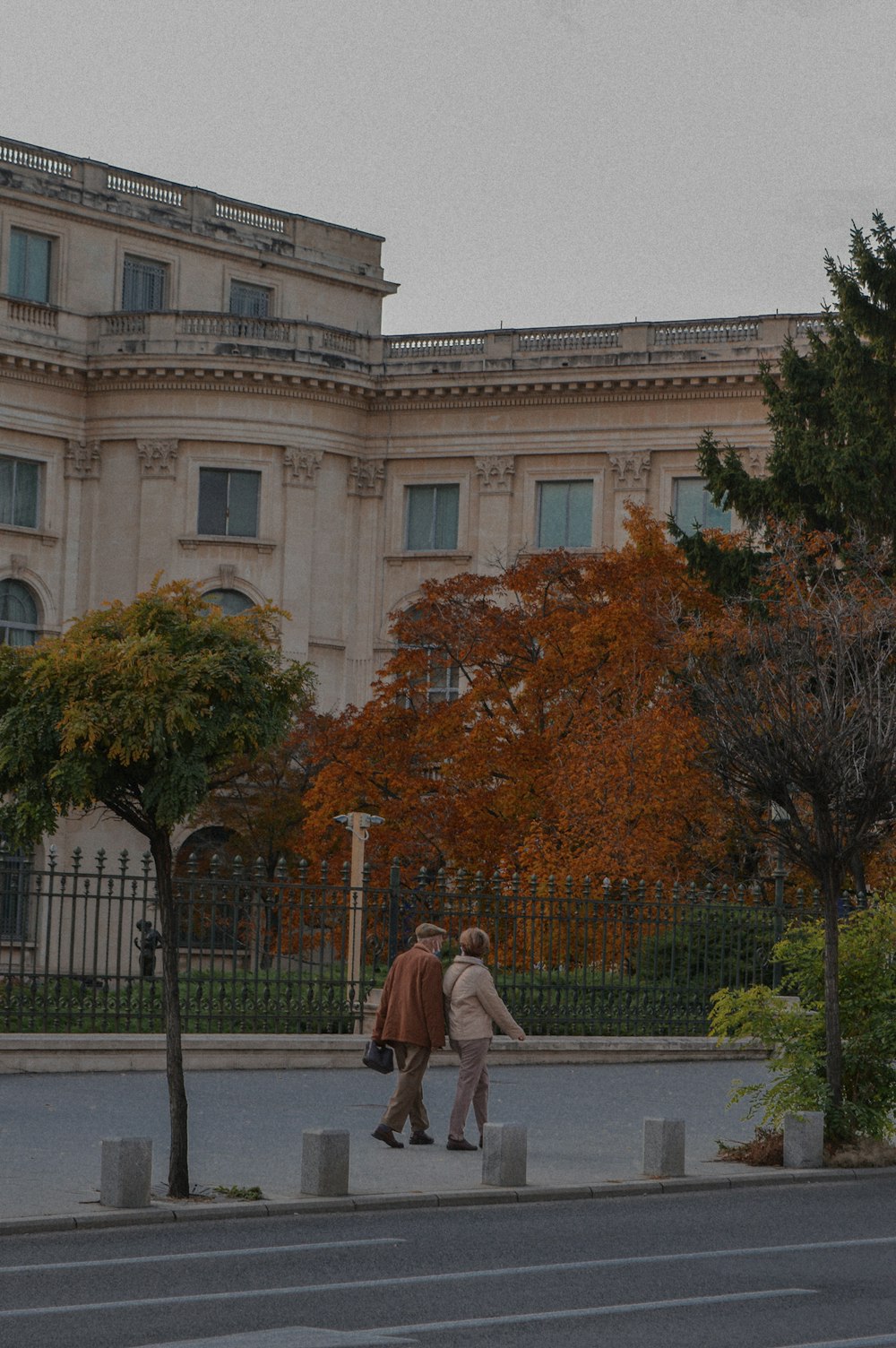 two people walking down the sidewalk in front of a large building