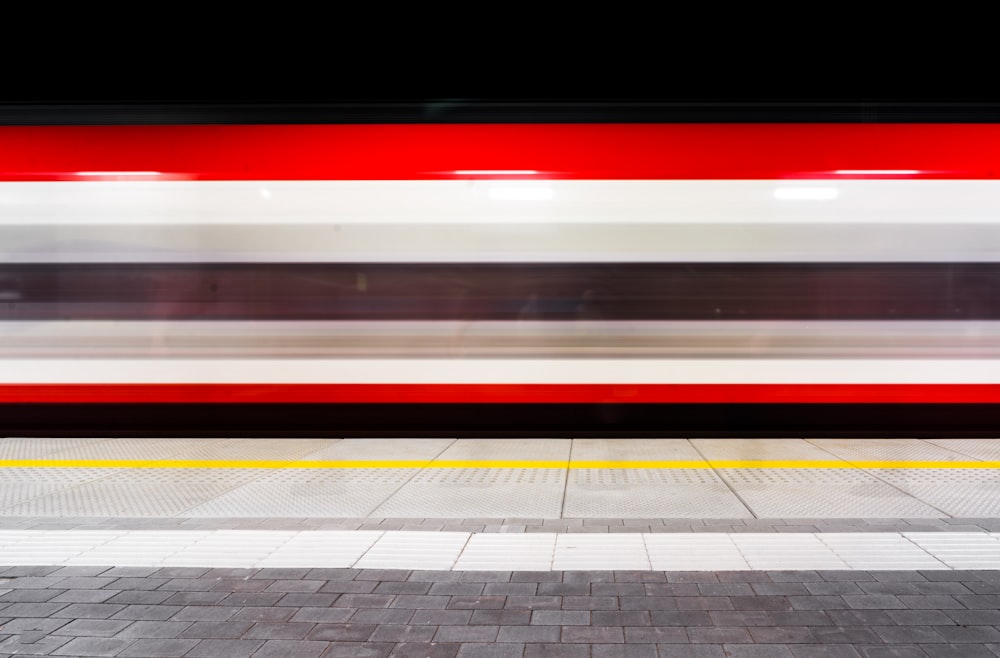 a red and white train passing by a platform