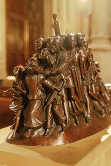 A detailed sculpture featuring a group of individuals intricately carved in a dynamic and expressive manner, showcasing a variety of poses and expressions. The figures appear to be of different ages and backgrounds, conveying unity and movement.