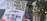 Protest signs are being held up in an outdoor setting with a background of trees and buildings. The signs include messages calling for an end to the conflict in Gaza and supporting a particular political stance.