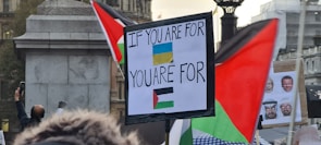 Close-up of a camera lens capturing a vibrant protest with blue flags.