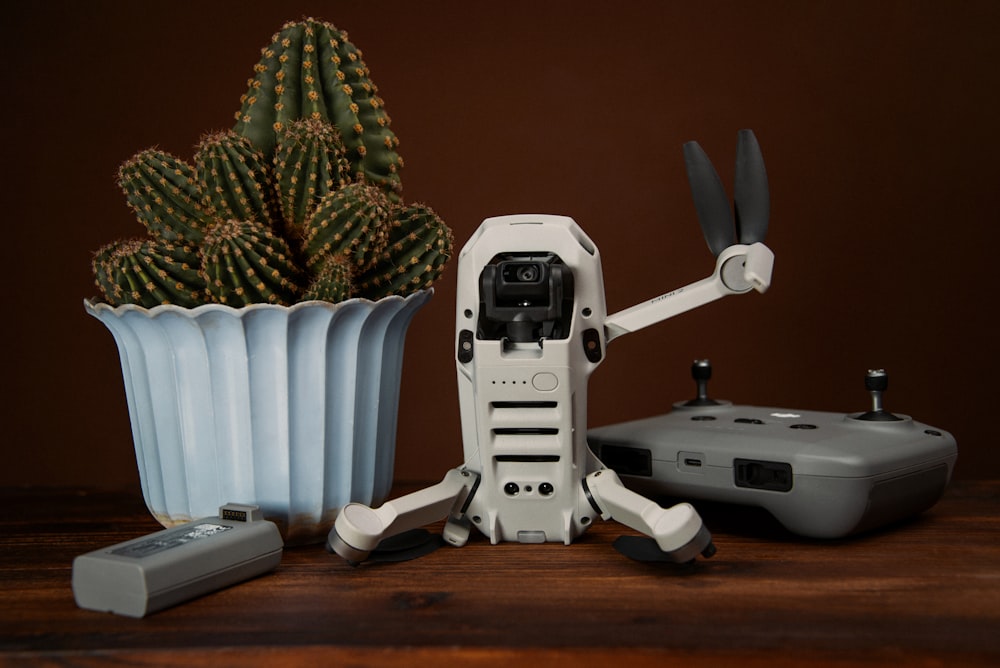 a robot holding a remote control next to a potted cactus