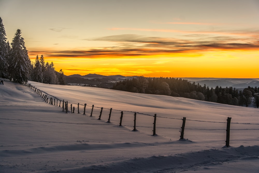a fence in the snow with a sunset in the background