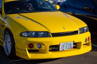 A bright yellow sports car with sleek design and aerodynamic features is parked in a lot. The car has distinctive blue lightning bolt decals along the sides and a custom license plate from Oregon. The front headlights are sleek and integrated into the body, while aftermarket wheels add to the sporty appeal.