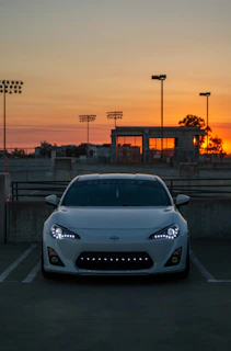 A sleek white luxury car parked elegantly at a sunset-lit event venue.