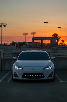 A sleek white luxury car parked elegantly at a sunset-lit event venue.