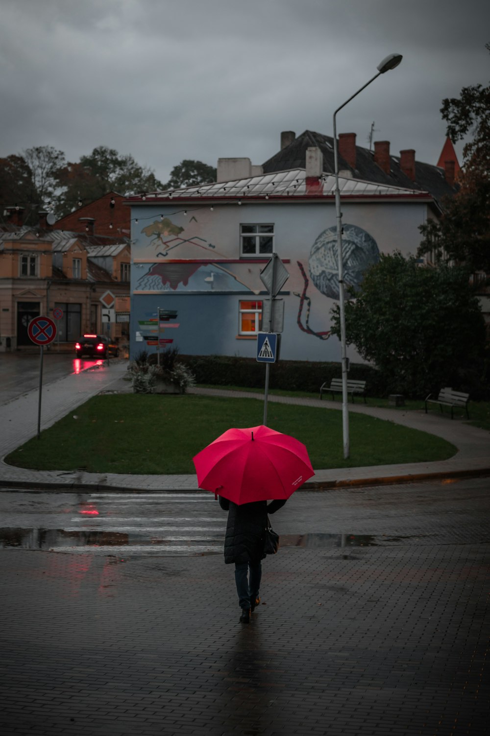 a person walking down a street holding a red umbrella