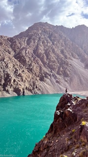 The creator of abjaustral standing on a rocky outcrop overlooking a turquoise glacial lake