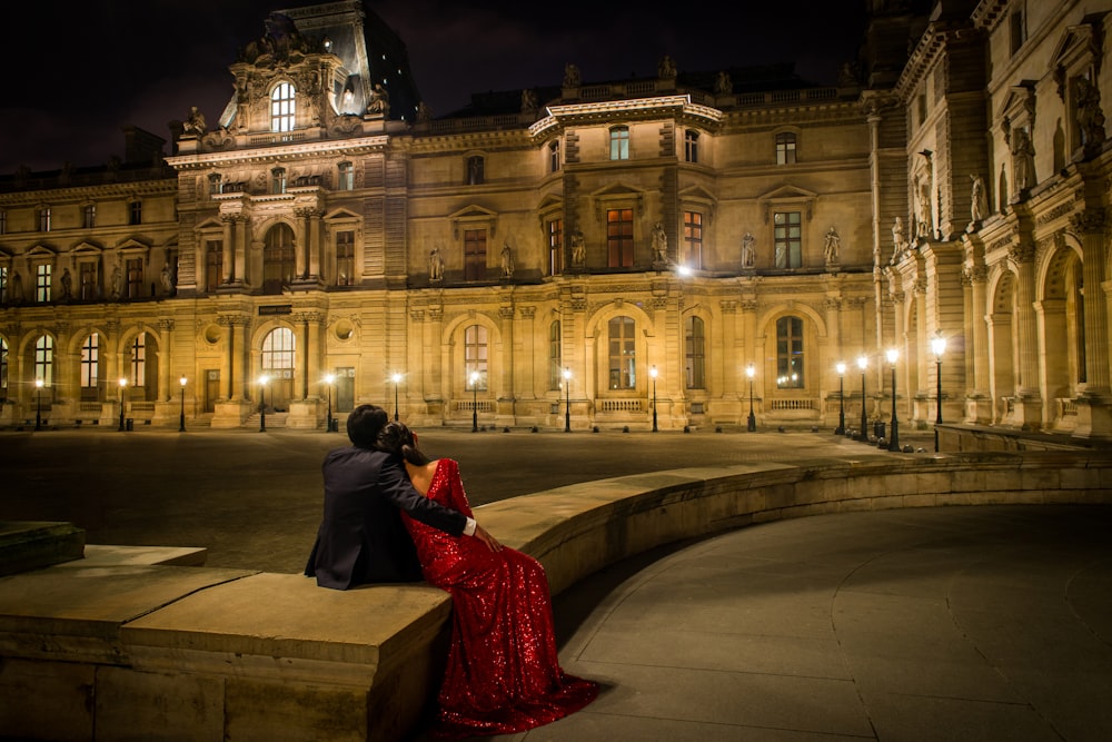 a man and a woman sitting on a ledge in front of a building