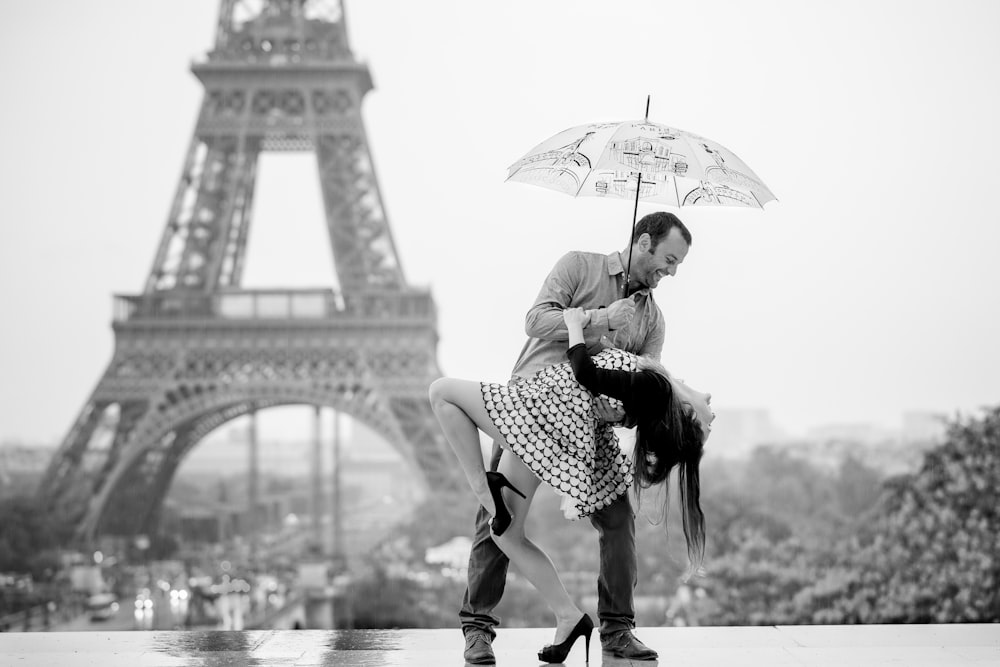 a man holding a woman under an umbrella in front of the eiffel tower
