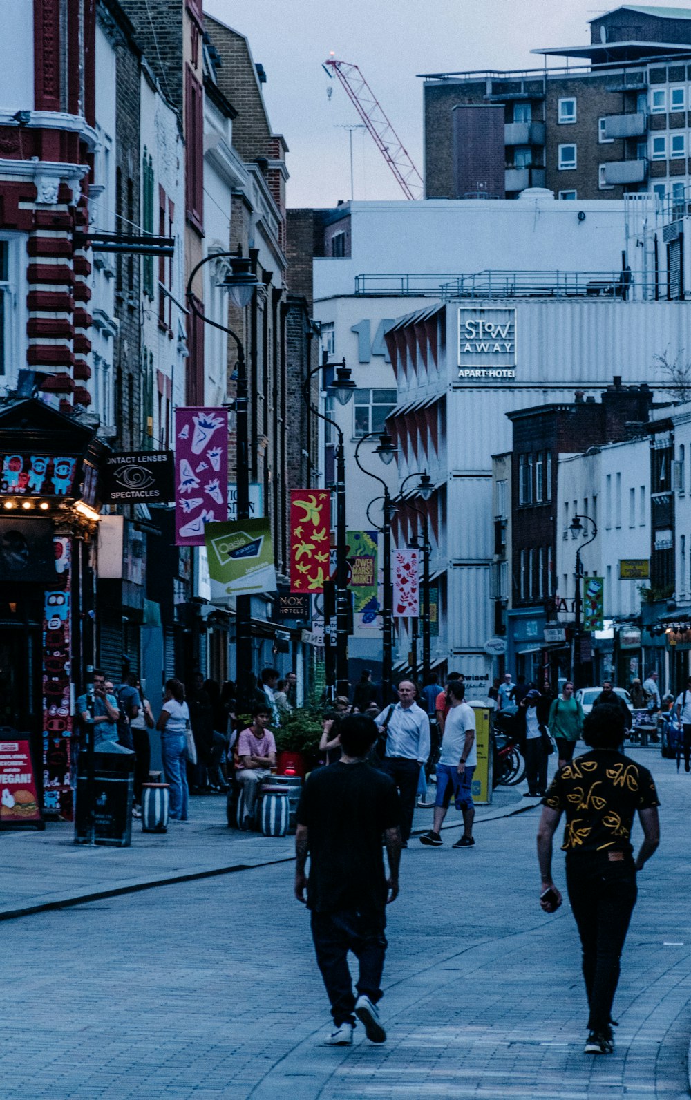 a group of people walking down a street next to tall buildings