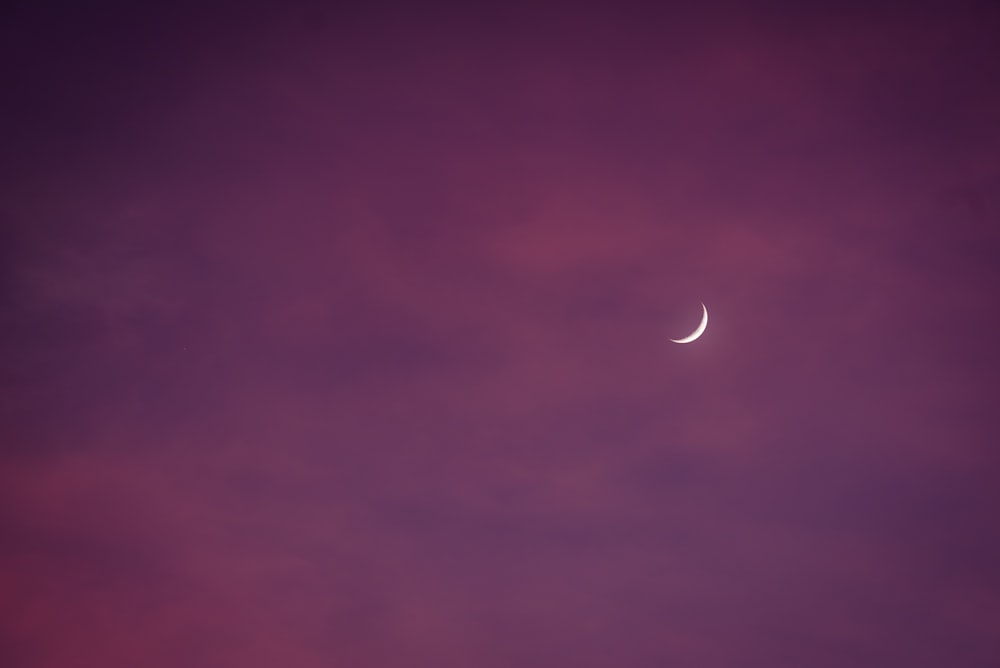 a crescent moon in a purple sky with clouds