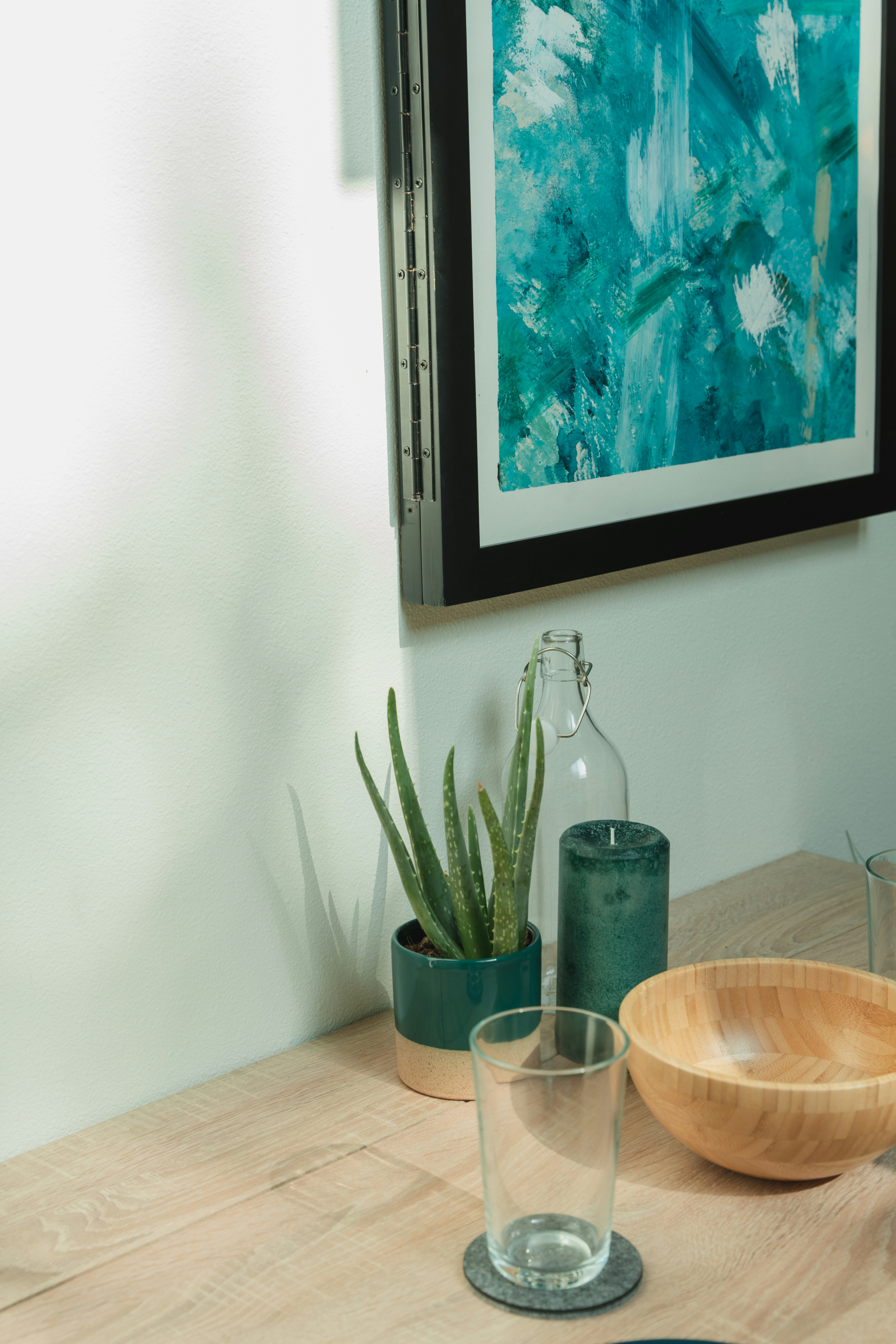 Explore the perfect dining ambiance with a table adorned by a plant, candle, bowl, and glass. The scene is elevated by an aesthetically pleasing wall art.