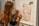 A person with long hair is writing notes on a whiteboard. Papers with diagrams and textual annotations are pinned to the board using wooden clips. The person appears focused and is using a pen to make annotations.