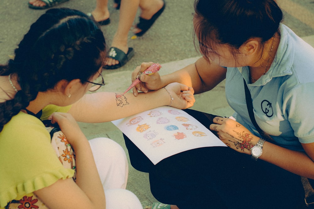 two girls sitting on the ground drawing on a piece of paper
