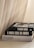 Three stacked fashion books with large, bold titles are placed near a soft, flowing curtain. The books feature grayscale covers with a modern, minimalist design.