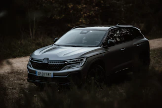 A sleek, luxury SUV waiting by a mountain road surrounded by lush greenery.