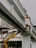 Two construction workers in bright orange safety vests and hats are standing on a raised platform attached to a crane arm, positioned on an elevated concrete bridge. The surroundings include urban infrastructure such as traffic lights and a building in the background. A height restriction sign indicating 4.5 meters is visible on the bridge.