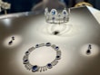 A display featuring a set of luxurious jewelry composed of a tiara, necklace, and earrings. Each piece is adorned with large, deep blue gemstones surrounded by intricate diamond settings, reflecting under the display lights.