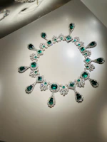 An elegant necklace with emerald gemstones displayed on a light wooden surface.