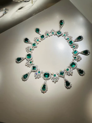 An elegant necklace with emerald gemstones displayed on a light wooden surface.