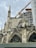 An ornate Gothic-style cathedral with pointed arches and stained glass windows is under renovation. A large construction crane and scaffolding are visible, indicating ongoing restoration work. The sky is overcast, enhancing the dramatic appearance of the architectural details.