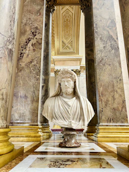 A marble bust of Aristotle with classical Greek columns in the background, bathed in soft golden light.