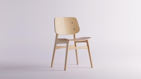 A minimalist wooden chair with a simple design, featuring a slightly curved backrest and seat. It has a light wood finish and is positioned against a plain, light background. The chair is made from smooth wooden materials with visible wood grain.