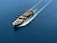 A cargo ship is sailing through a vast expanse of blue water, carrying numerous colorful shipping containers. The ship leaves a trail of waves behind, slicing smoothly through the calm sea.