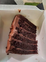A transparent cake box revealing a layered chocolate and gold-themed luxury cake.