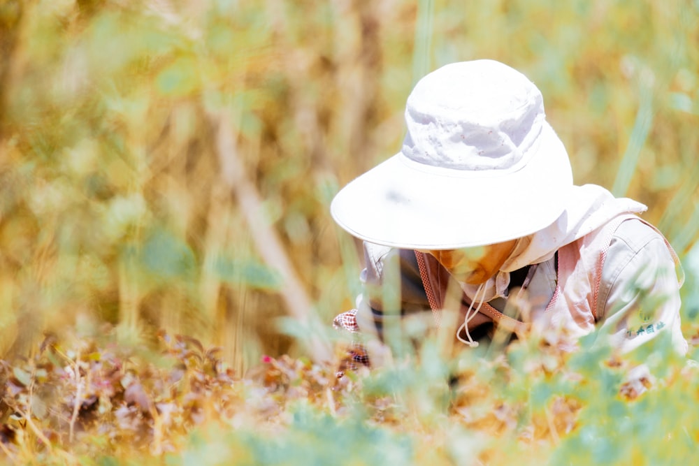 a woman wearing a white hat crouches in a field